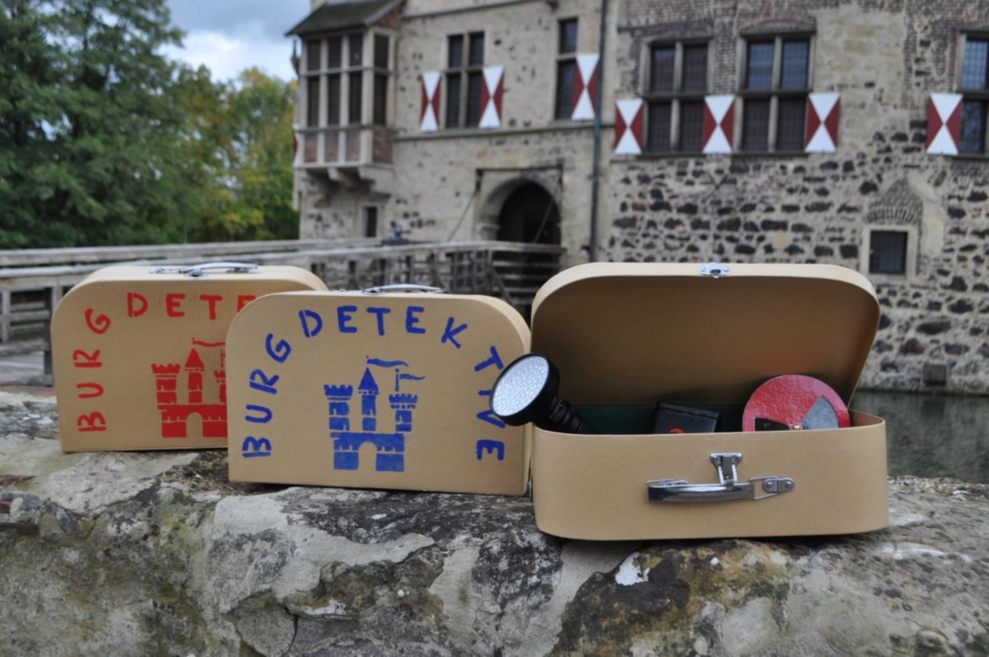 Köfferchen mit Werkzeugen für die Detektivarbeit liegen auf der Mauer im Innenhof der Burg Vischering.