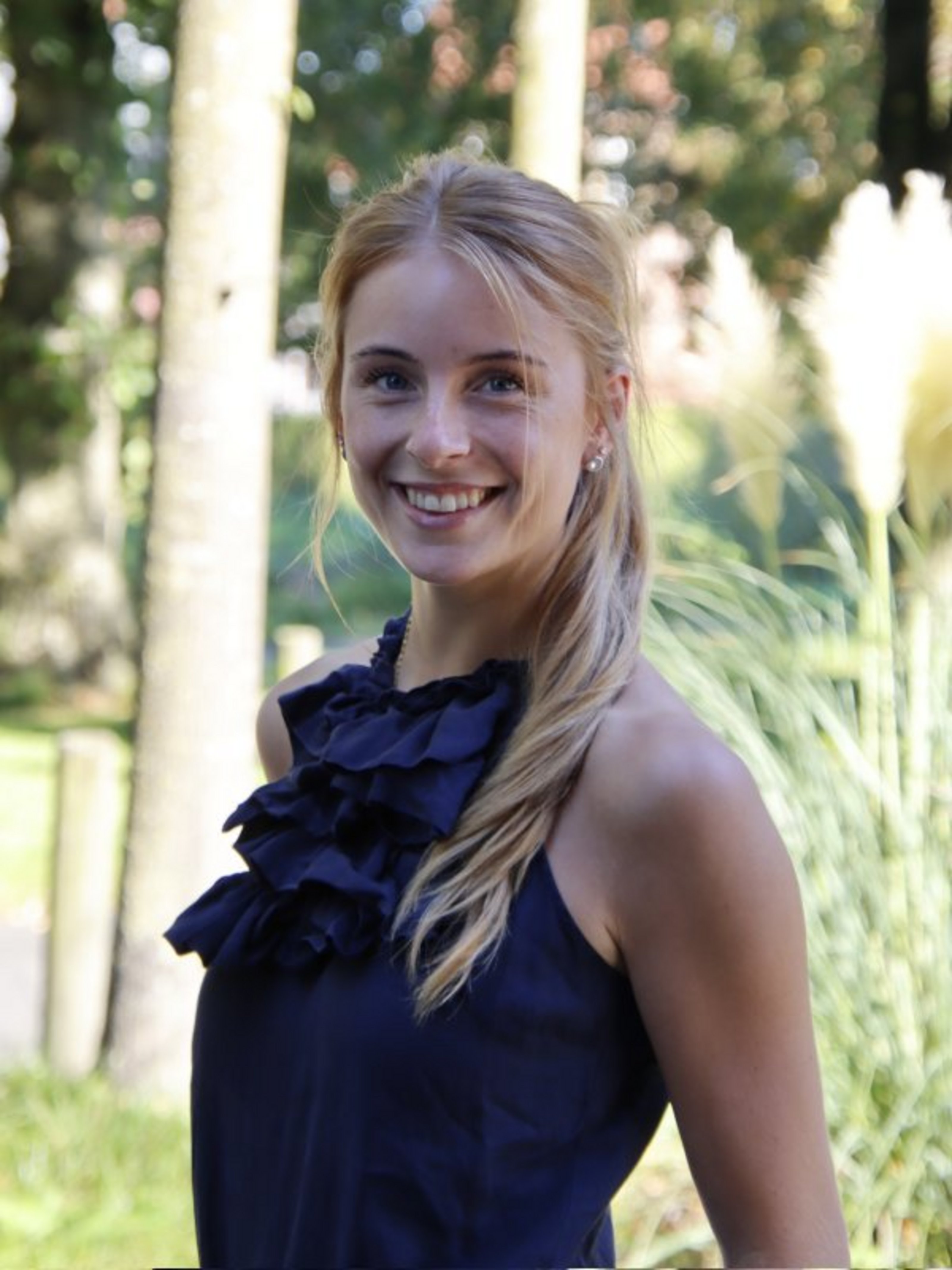 Ein Porträtbild mit der Ansprechpartnerin Paulina Risthaus. Sie trägt eine blaues Kleid und steht vor einigen Bäumen.
